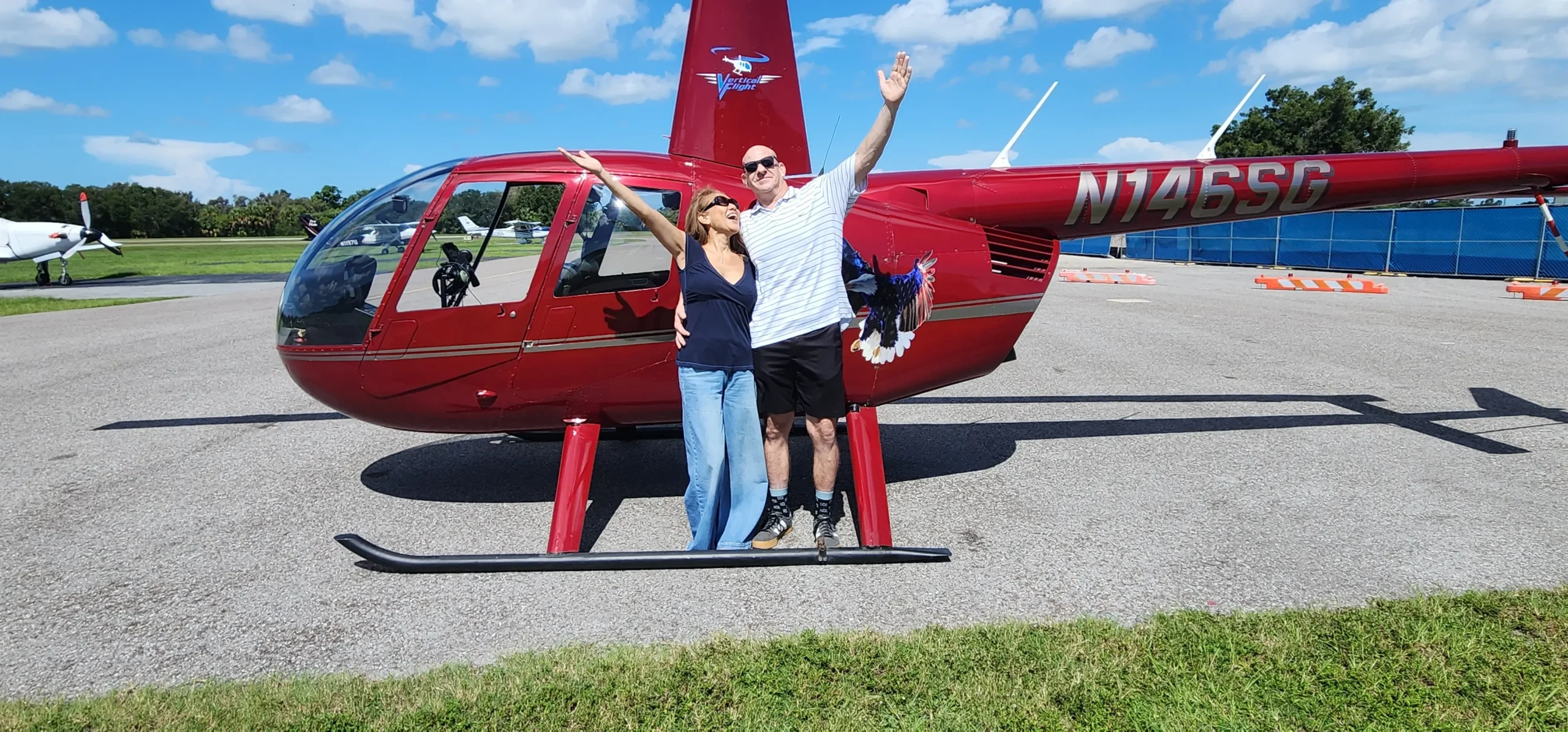 Happy Vertical Flight guests celebrating beside a red helicopter at Clearwater Airpark